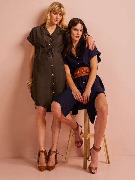 2 vrouwen waarvan 1 staand en 1 zittend op een krukje die allebei een overhemd jurk dragen