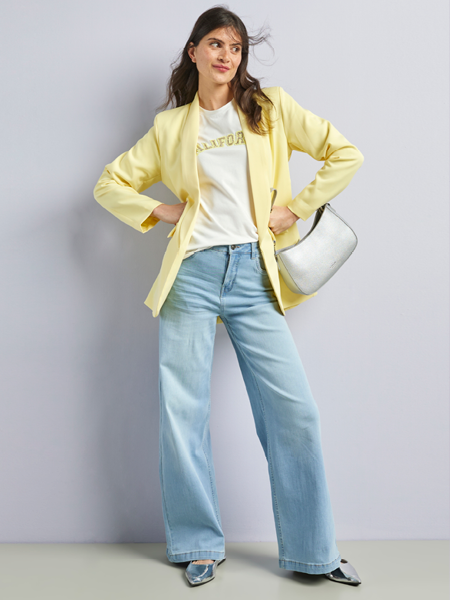 vrouw staand met een wide fit jeans en gele blazer met handen in heupen