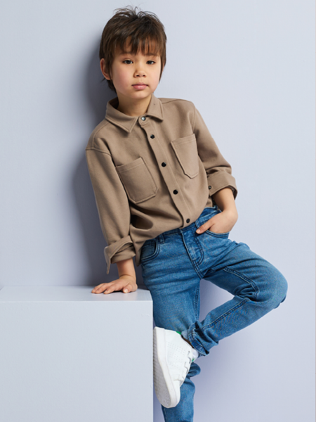 jongen met een bruine blouse op een donkerblauwe jeans