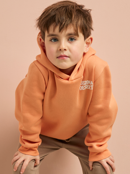 jongen met een oranje trui op een bruine broek