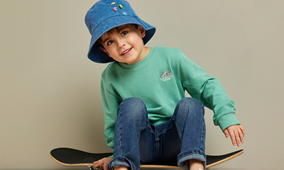 jongen op een skateboard met een groen shirt, donkerblauwe jeans en blauw vissershoedje