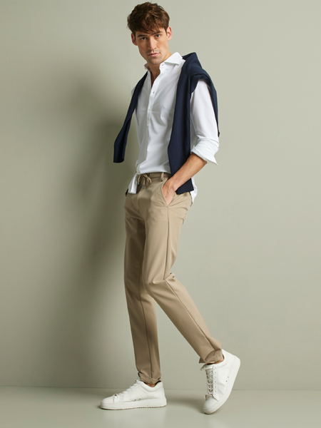 man in beige chino met wit overhemd en een trui over de schouders
