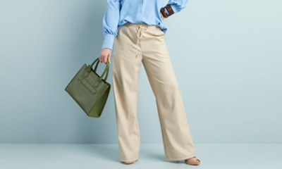 vrouw met nette beige wijde pantalon met een lichte blouse en groene handtas